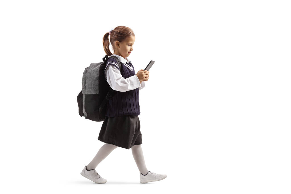 Küçük liseli kız akıllı bir telefonla yürüyor ve daktilo ediyor. - Fotoğraf, Görsel