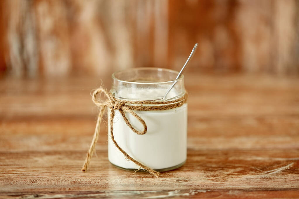 jogurtti tai smetana lasipurkissa puupöydällä
 - Valokuva, kuva