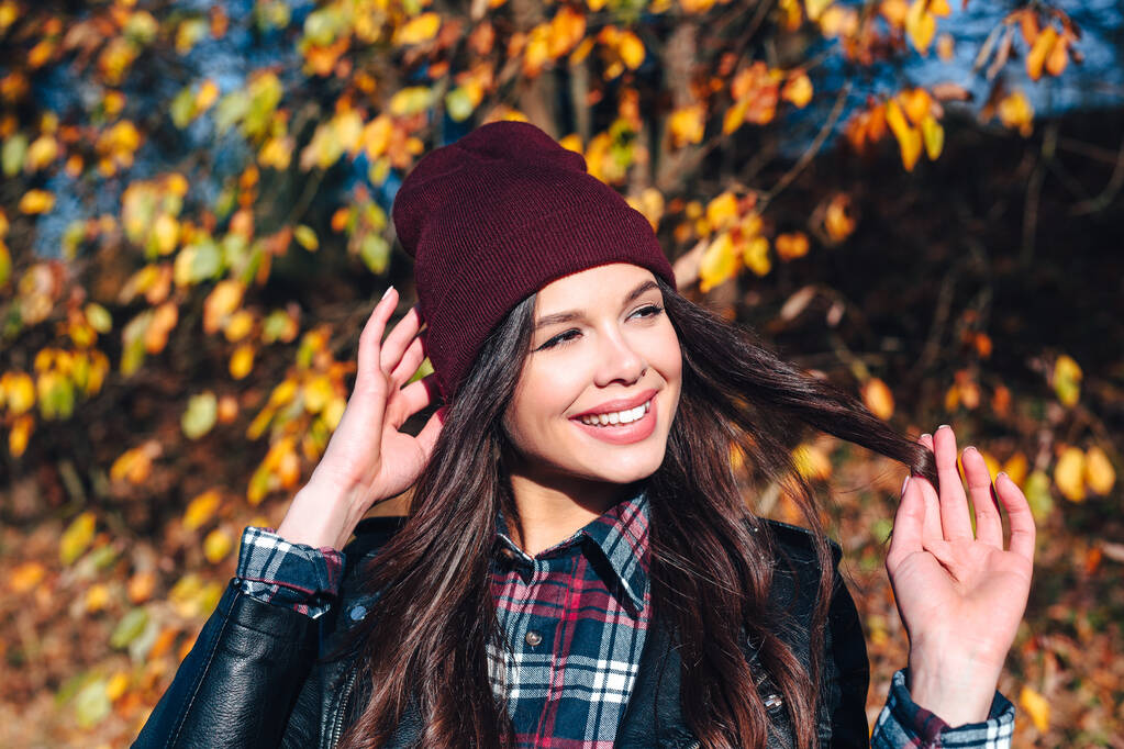 Elegante joven con un sombrero y una camisa a cuadros en el parque de otoño en un día soleado - Foto, imagen