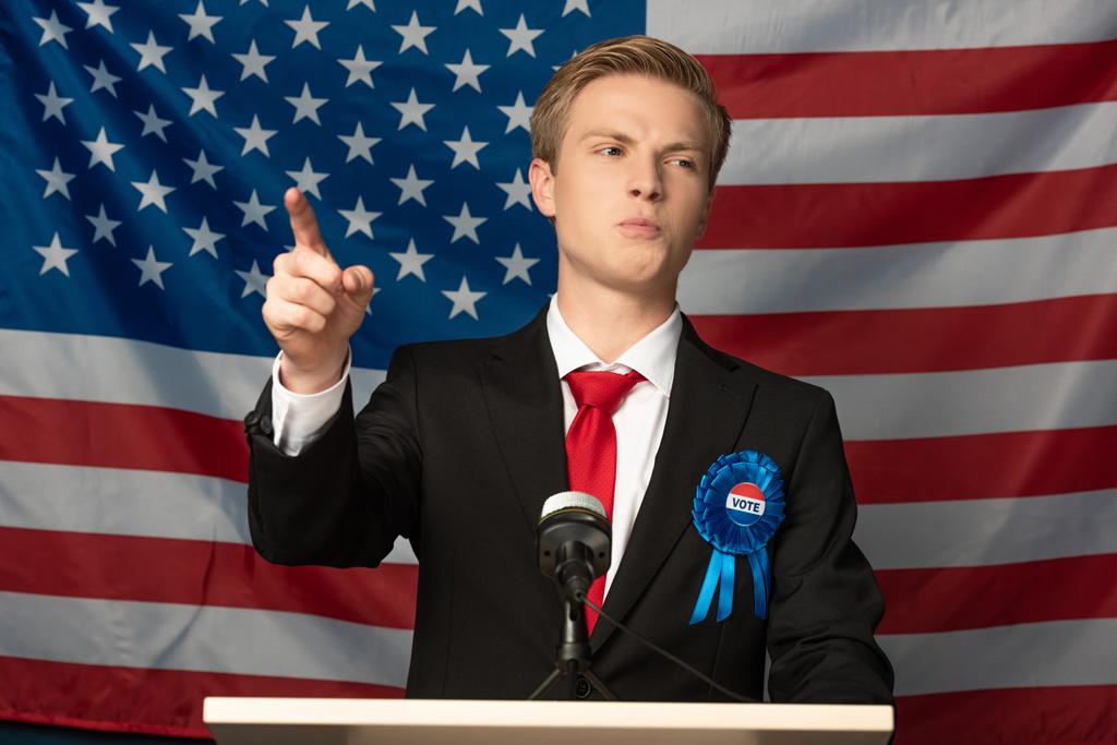 συναισθηματικός άνθρωπος που δείχνει με το δάχτυλο σε tribune στην αμερικανική σημαία φόντο - Φωτογραφία, εικόνα