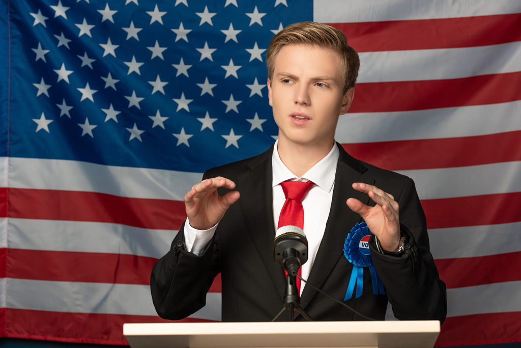 hombre emocional en tribuna durante discurso sobre fondo de bandera americana
 - Foto, Imagen