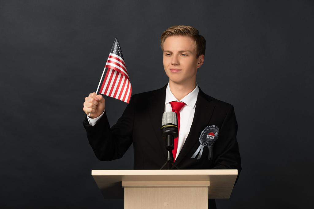 Siyah arka planda Amerikan bayrağıyla Tribünde gülümseyen duygusal adam - Fotoğraf, Görsel