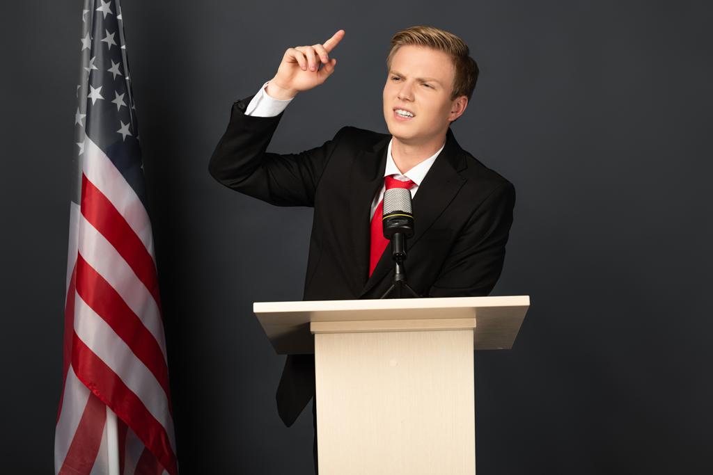 συναισθηματικός άνθρωπος μιλώντας σε tribune με αμερικανική σημαία σε μαύρο φόντο - Φωτογραφία, εικόνα