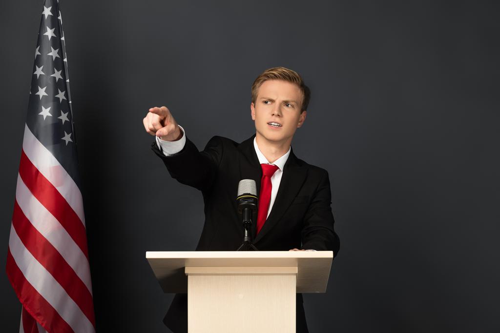 emocjonalny mężczyzna wskazując palcem na trybunie z amerykańską flagą na czarnym tle - Zdjęcie, obraz