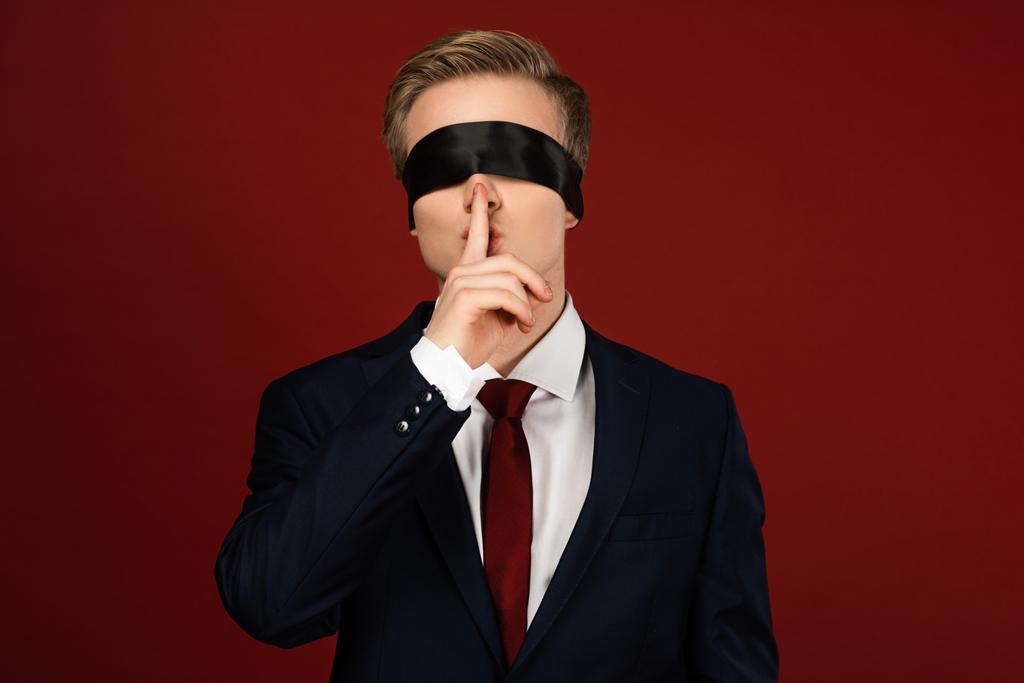 férfi bekötött szemmel mutatja shh gesztus piros háttér - Fotó, kép