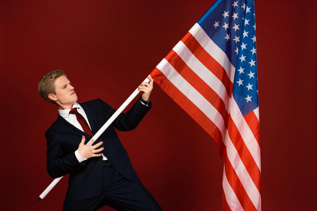 емоційний чоловік тримає американський прапор на червоному тлі
 - Фото, зображення