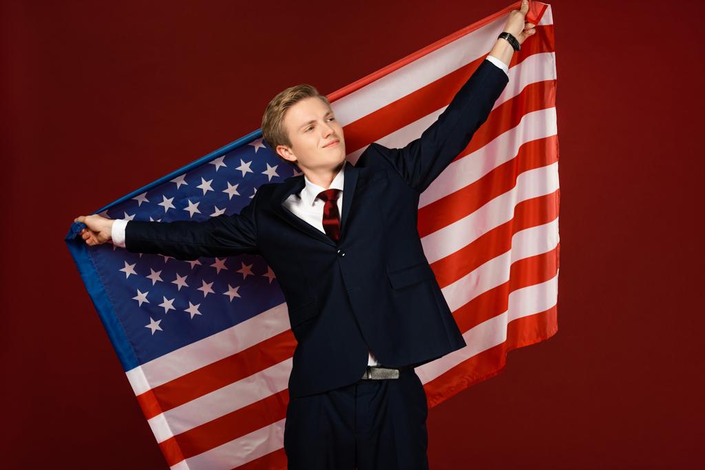 Lächelnder Mann mit amerikanischer Flagge auf rotem Hintergrund - Foto, Bild