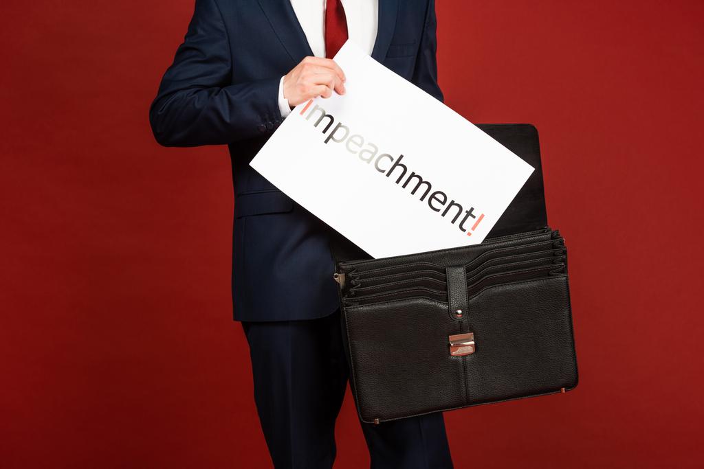 vista recortada del hombre tomando tarjeta blanca con letras de juicio político de la caja de cuero sobre fondo rojo
 - Foto, Imagen