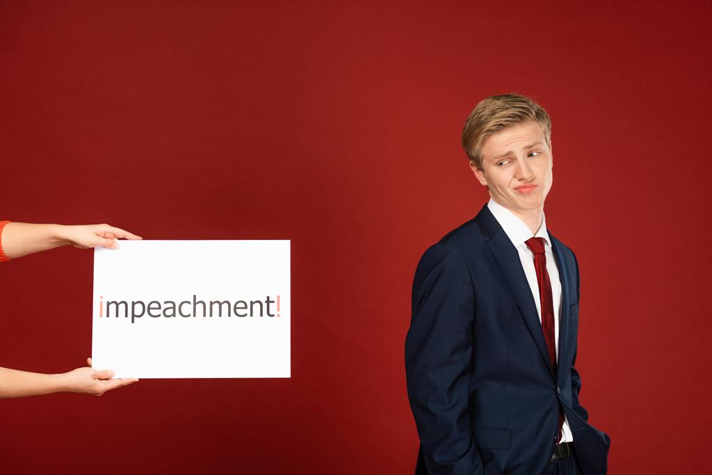 skeptical man near white card with impeachment lettering on red background - Photo, Image