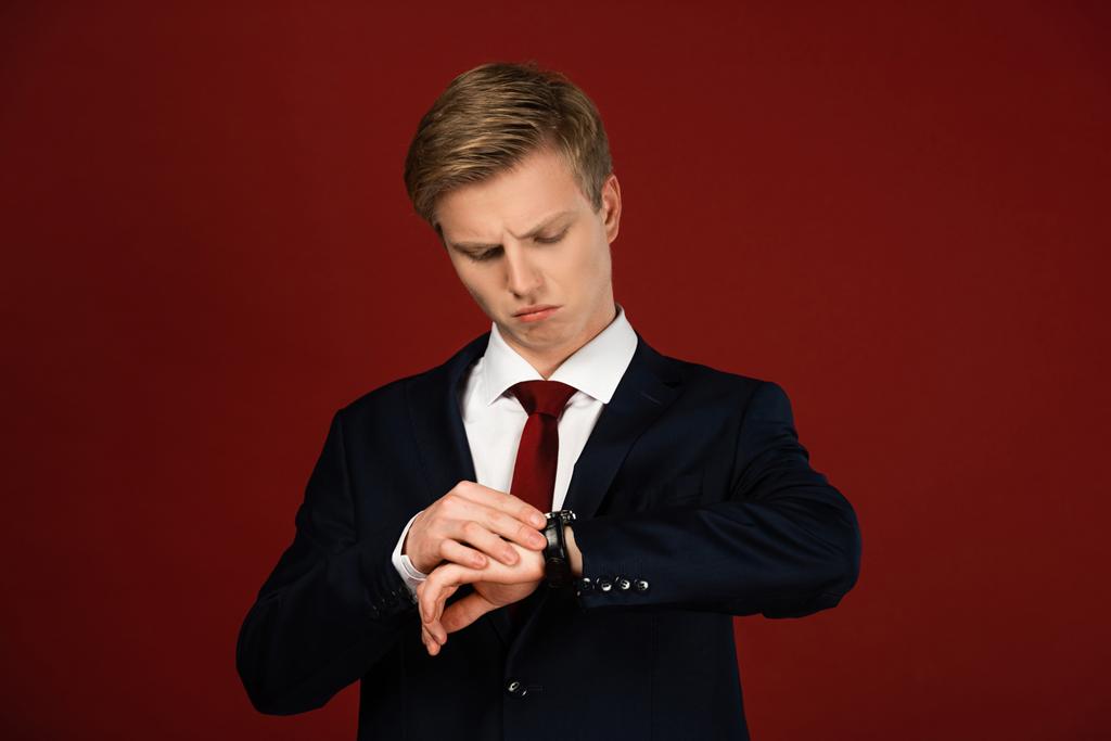 мужчина смотрит на наручные часы на красном фоне
 - Фото, изображение