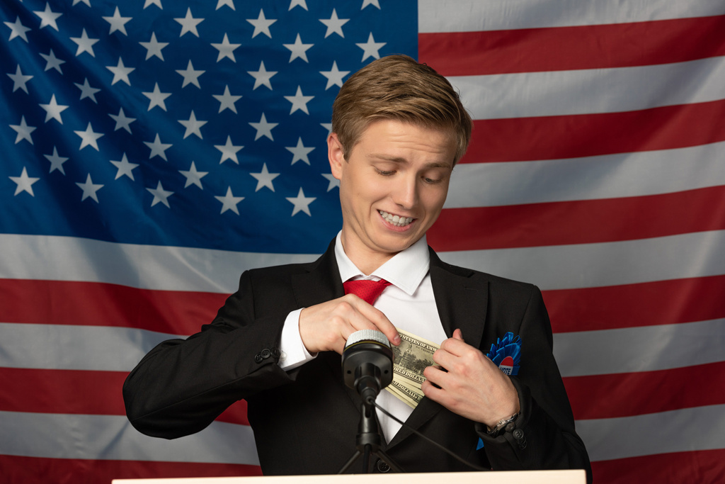человек, держащий деньги на трибуне на фоне американского флага
 - Фото, изображение