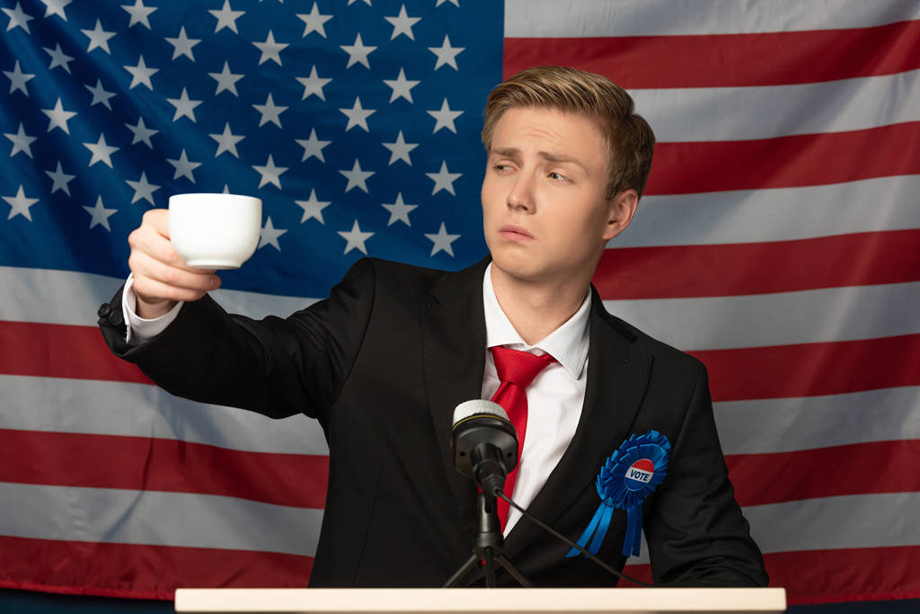 man looking at coffee cup on tribune on american flag background - Photo, Image