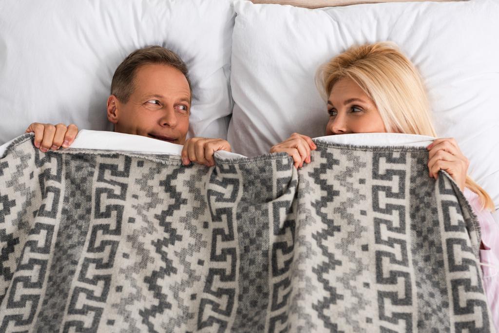 Visão superior do casal cobrindo com cobertor e olhando um para o outro
 - Foto, Imagem