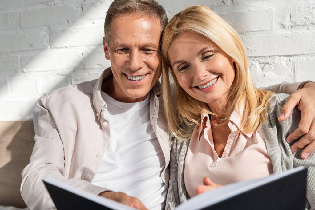 Lächelndes Paar blickt auf Notizbuch und Mann umarmt Frau - Foto, Bild