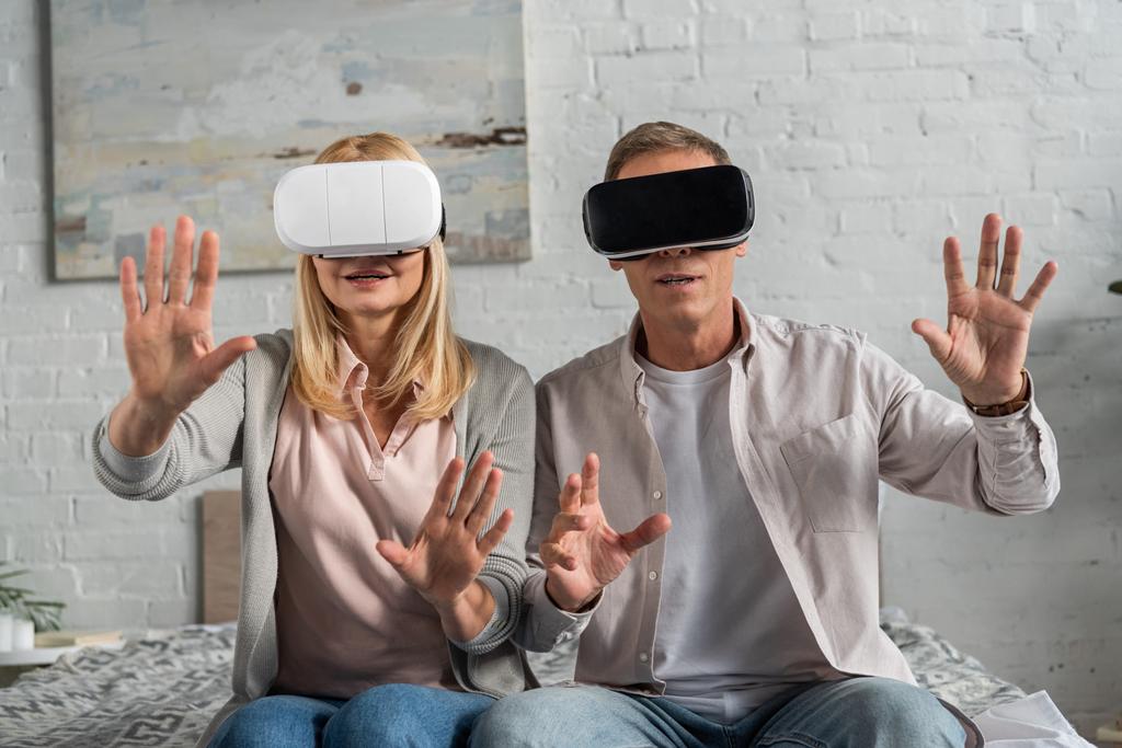 Paar in Virtual-Reality-Headsets spielt Videospiel und gestikuliert im Bett - Foto, Bild