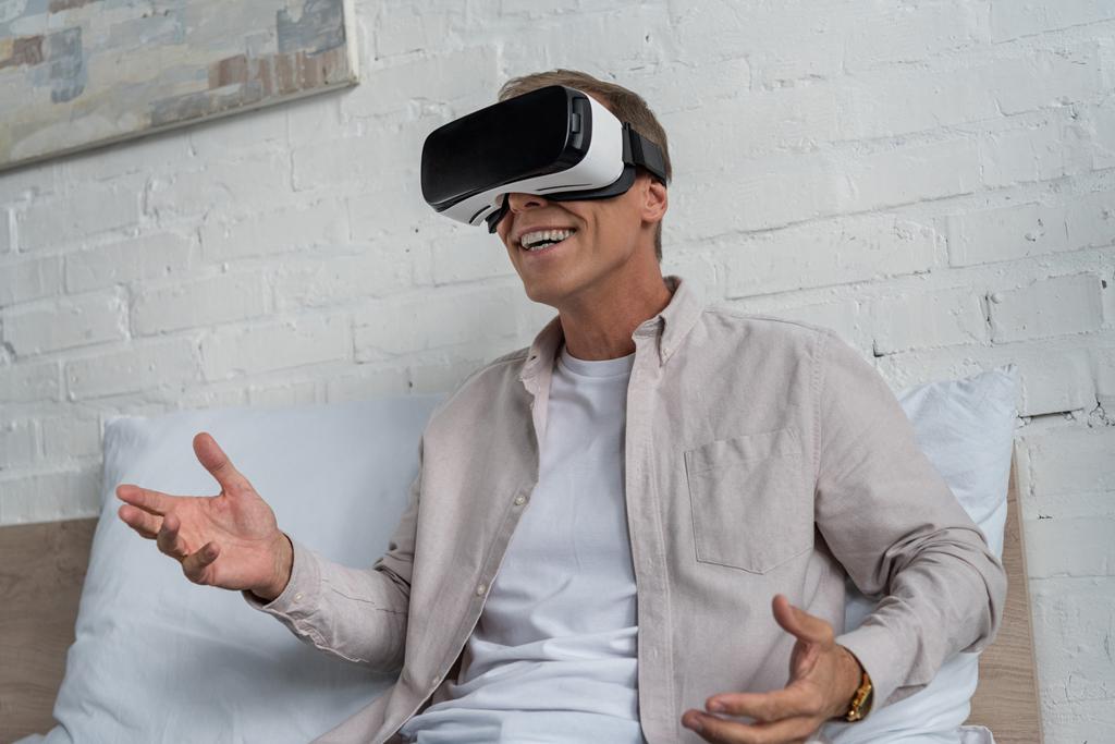 Glimlachende man in virtual reality headset videospel spelen op bed - Foto, afbeelding