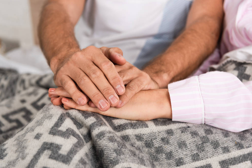 Vista cortada do casal de mãos dadas em cobertor na cama
 - Foto, Imagem