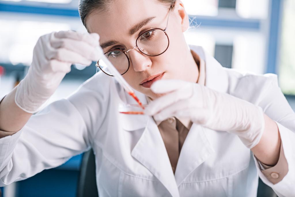 selective focus of attractive immunologist holding pipette with red liquid in laboratory  - Photo, Image