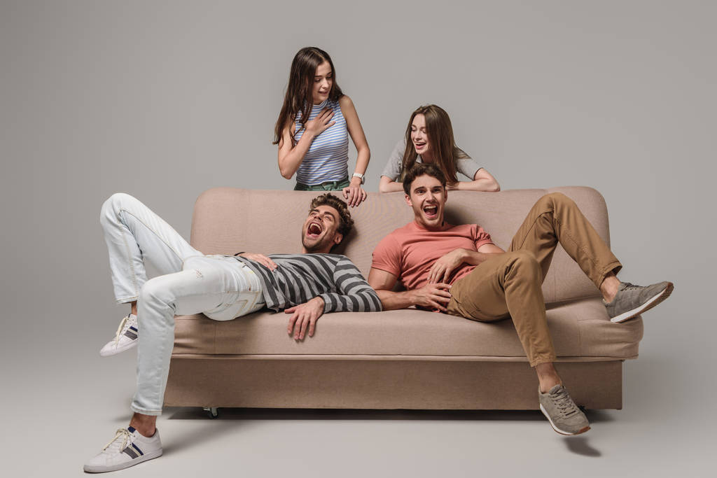 молоді друзі сміються і розслабляються на дивані на сірому
  - Фото, зображення