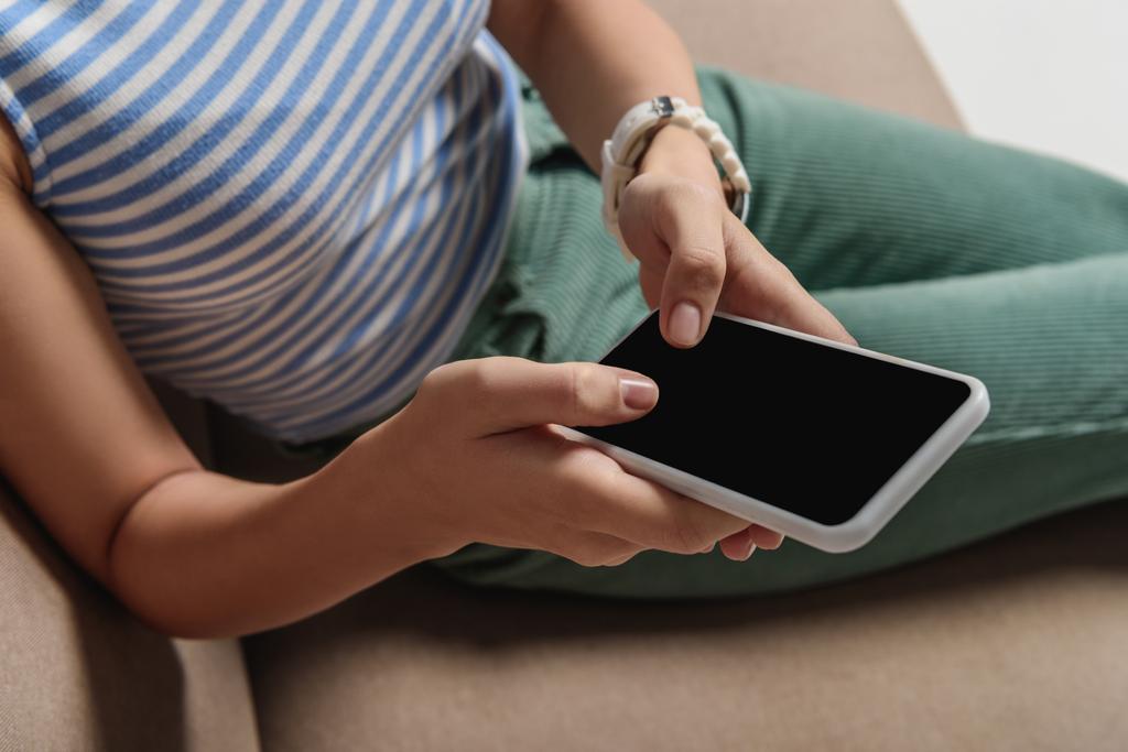 rajattu näkymä nainen käyttää älypuhelinta tyhjällä näytöllä istuessaan sohvalla
 - Valokuva, kuva