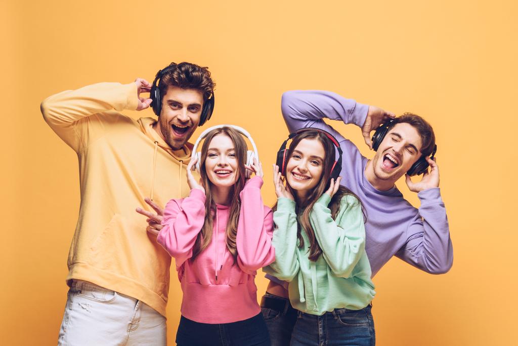 smiling friends listening music in headphones and dancing together, isolated on yellow - Photo, Image
