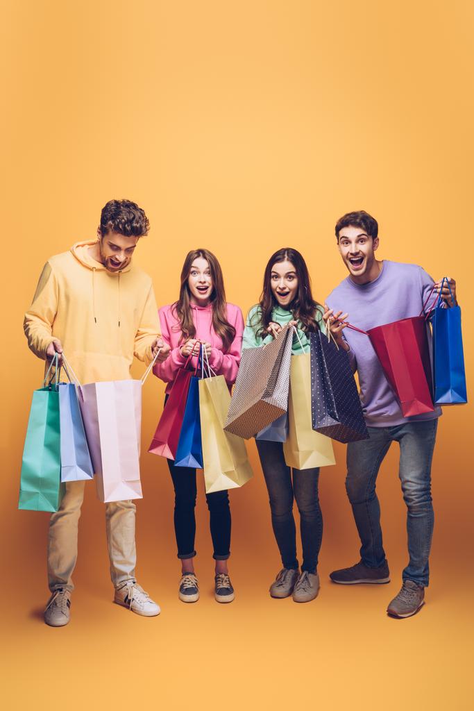 surprised young friends holding shopping bags together, on yellow - Photo, Image