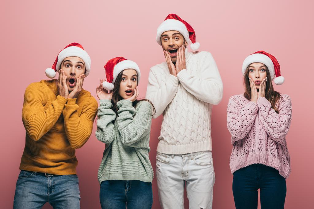 überraschte Freunde in Pullovern und Weihnachtsmützen, isoliert auf rosa - Foto, Bild