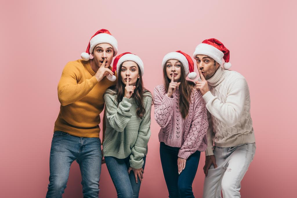 happy friends in sweaters and santa hats showing silence symbols, isolated on pink - Photo, Image
