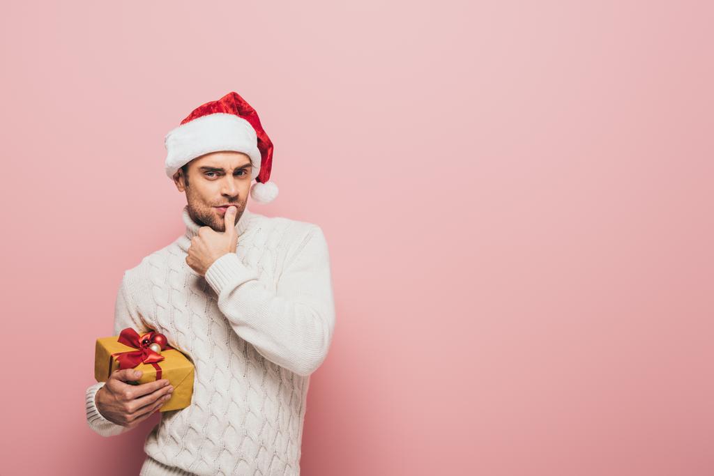 hombre reflexivo en suéter y sombrero de santa celebración de Navidad presente, aislado en rosa
 - Foto, imagen
