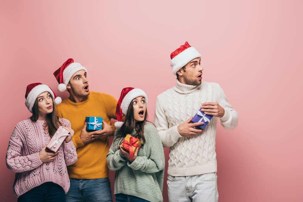 shocked friends in santa hats holding christmas presents, isolated on pink - Photo, Image