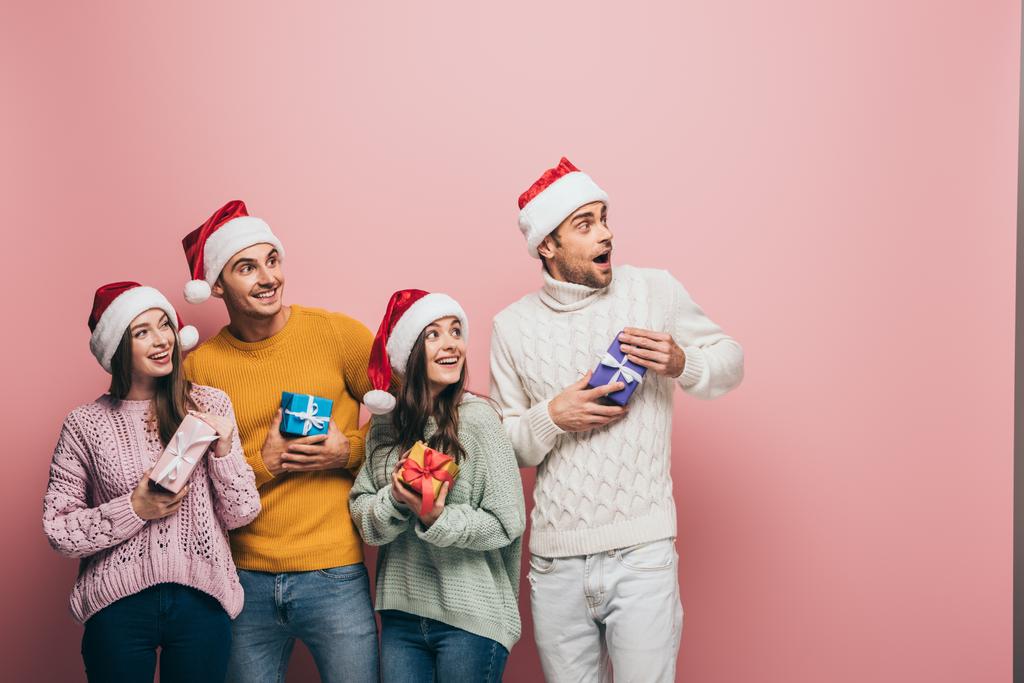 glückliche Freunde in Weihnachtsmützen mit Weihnachtsgeschenken, isoliert auf rosa - Foto, Bild