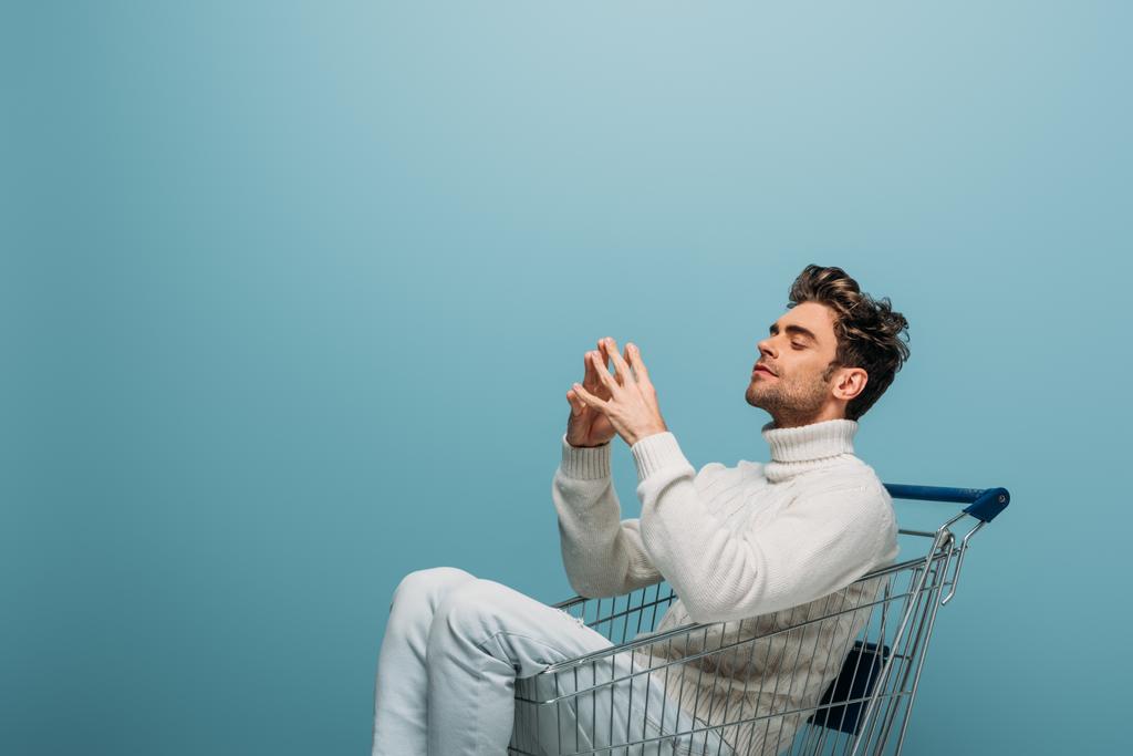 nachdenklicher Mann sitzt im Einkaufswagen, isoliert auf blauem Grund - Foto, Bild