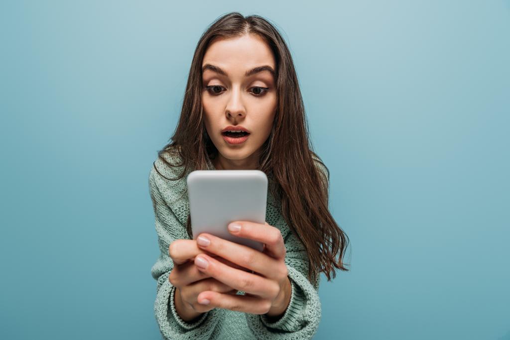 surprised girl using smartphone, isolated on blue - Photo, Image