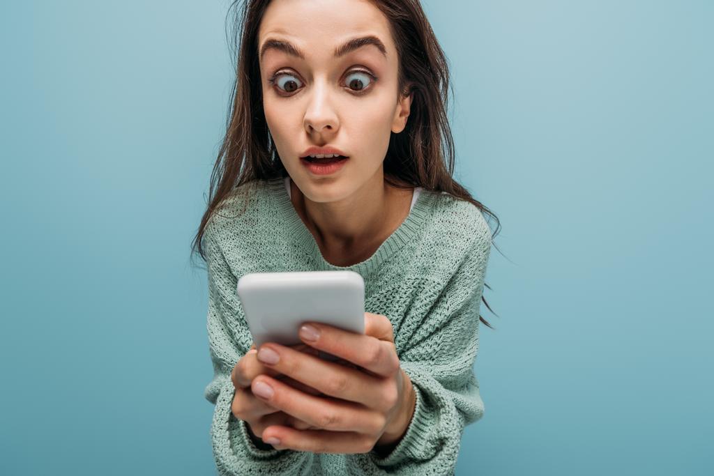 шокована жінка дивиться на смартфон, ізольована на синьому
 - Фото, зображення