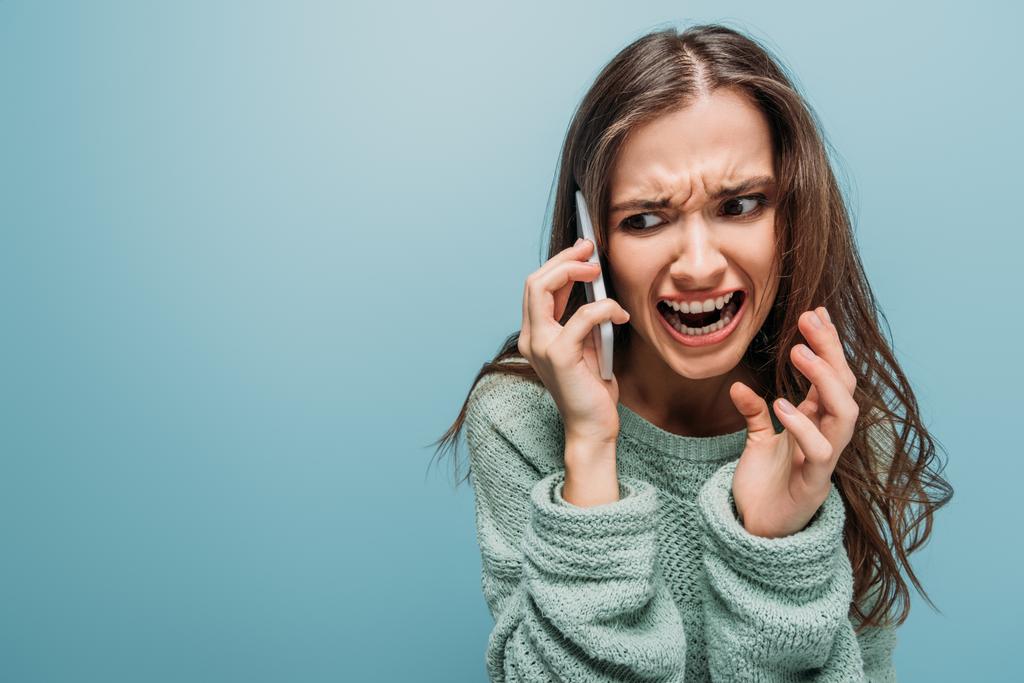 aggressive woman screaming and talking on smartphone, isolated on blue - Photo, Image