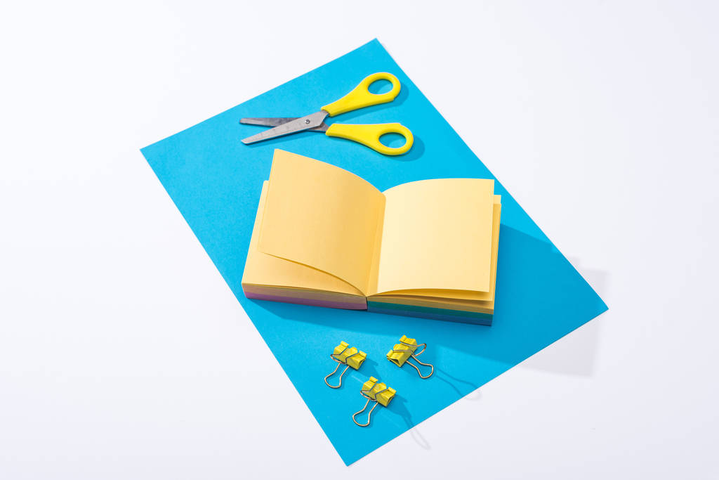 high angle view of notebook, scissors, binder clips and paper on white background  - 写真・画像