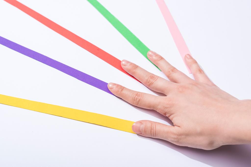 oříznutý pohled na ženu dotýkající se barevných papírových pruhů na bílém pozadí - Fotografie, Obrázek