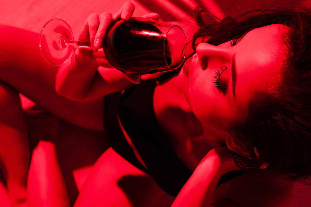 mooi sensueel meisje met glas wijn zitten in keuken in rood licht  - Foto, afbeelding