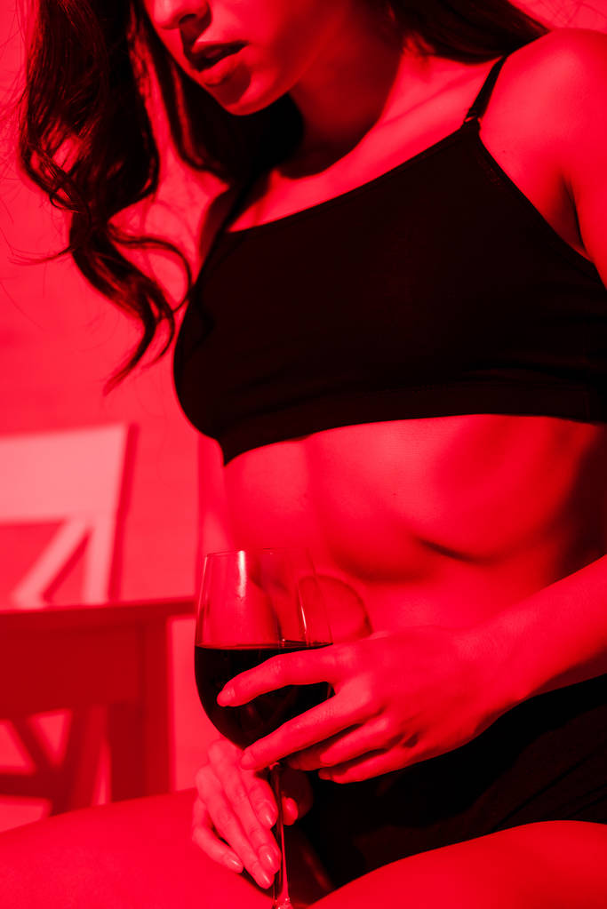 赤の光の中でキッチンにワインのガラスとセクシーな女の子のクロップドビュー  - 写真・画像