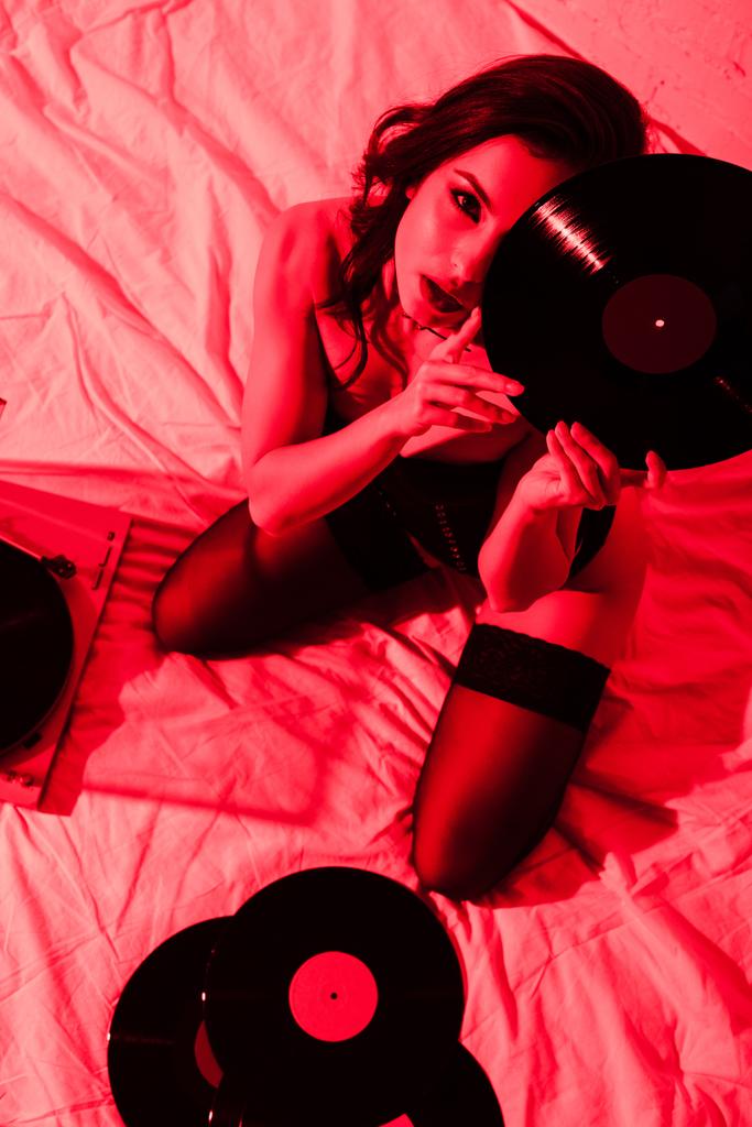 mooie gepassioneerde vrouw zittend op bed met vinyl platen in rood licht - Foto, afbeelding