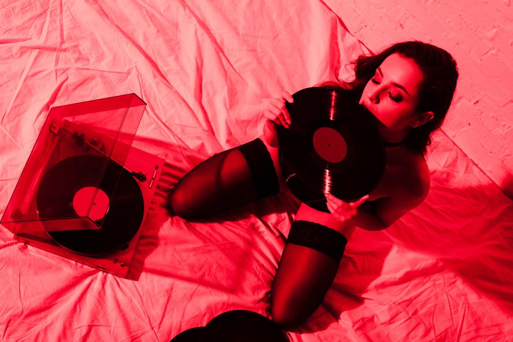 attractive seductive girl sitting on bed with vinyl records in red light - Photo, Image