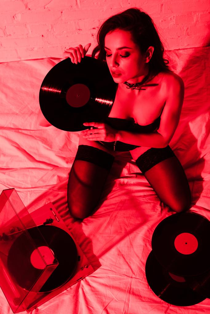 sexy Frau in Strümpfen sitzt auf dem Bett mit Schallplatten im Rotlicht - Foto, Bild
