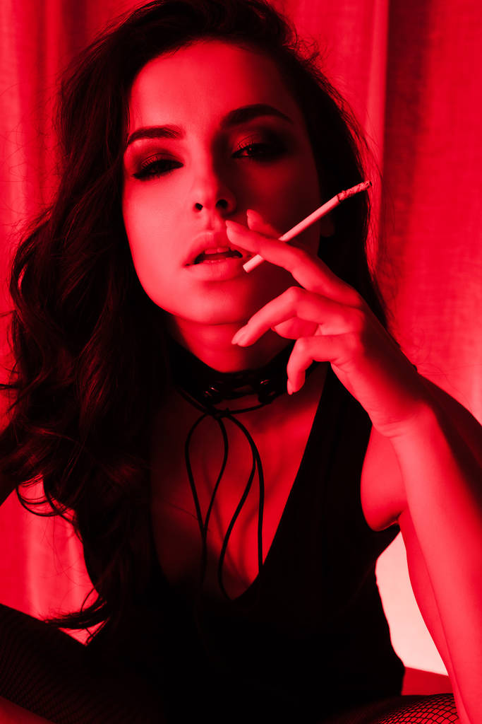 Kırmızı ışıkta sigara içen çekici, şehvetli kız. - Fotoğraf, Görsel