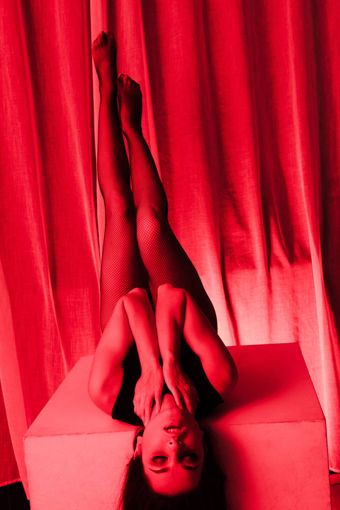 atraktivní sexy žena pózující v bodysuit a síťované punčocháče v červeném světle - Fotografie, Obrázek