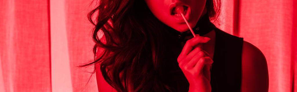 vue recadrée d'une jolie fille passionnée mangeant de la sucette dans la lumière rouge, plan panoramique
 - Photo, image