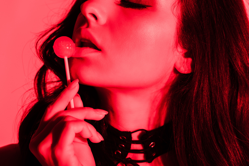 atrakcyjna uwodzicielska kobieta jedząca lizaka w czerwonym świetle - Zdjęcie, obraz