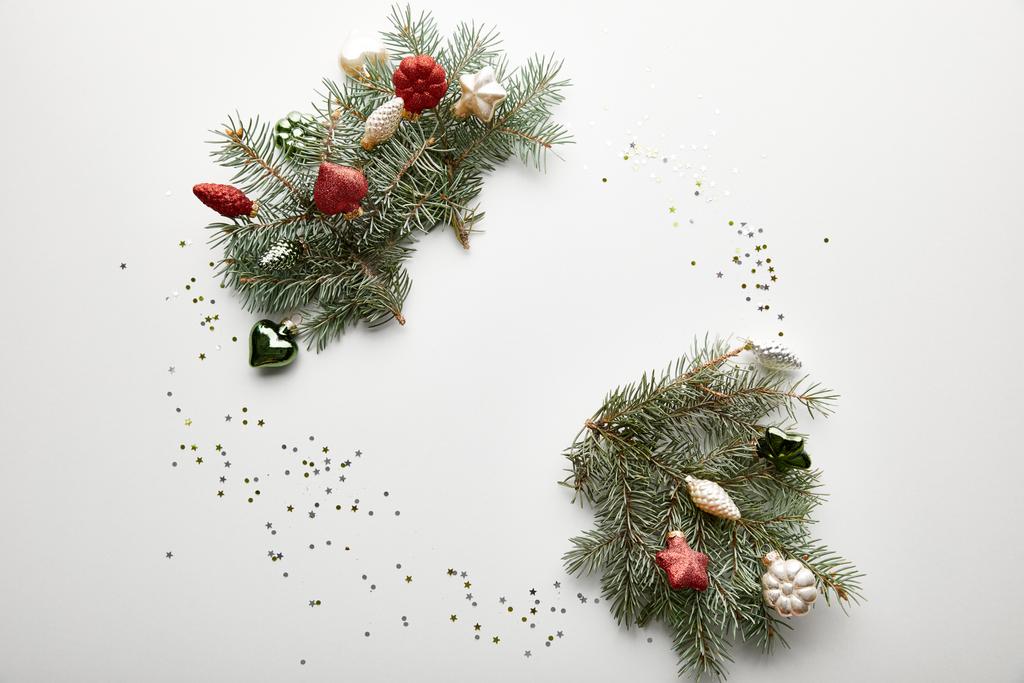 widok z góry świąteczne Boże Narodzenie ozdobione gałązki sosnowe z bombkami i konfetti na białym tle - Zdjęcie, obraz