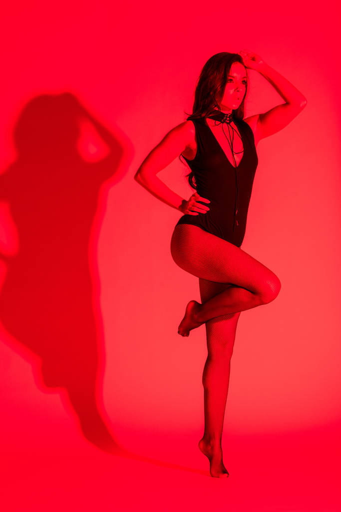 όμορφη παθιασμένη νεαρή γυναίκα ποζάρουν σε μαύρο κολάν, απομονωμένη σε κόκκινο - Φωτογραφία, εικόνα