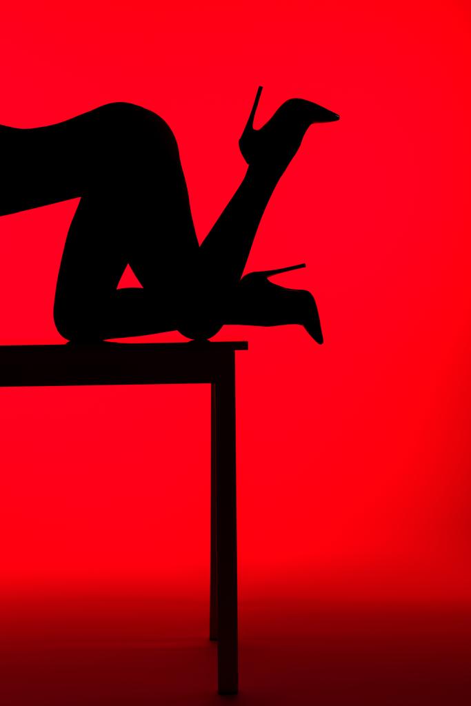 black silhouette of passionate woman in heels posing on table isolated on red - Photo, Image