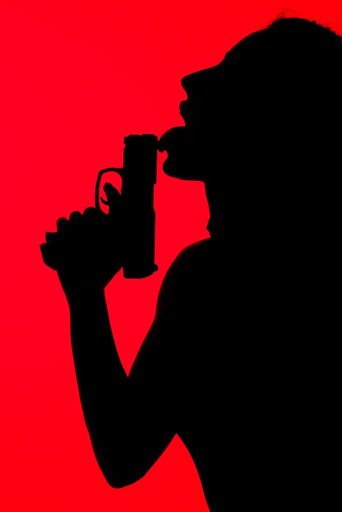 silhouette of criminal seductive woman licking gun isolated on red - Photo, Image